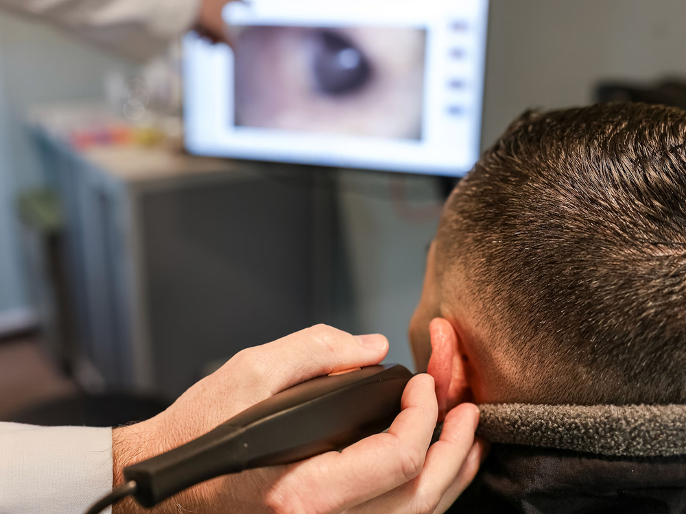 Doctor of Audiology examining a patient's ear canal before professional earwax removal at Precision Hearing in San Antonio, TX